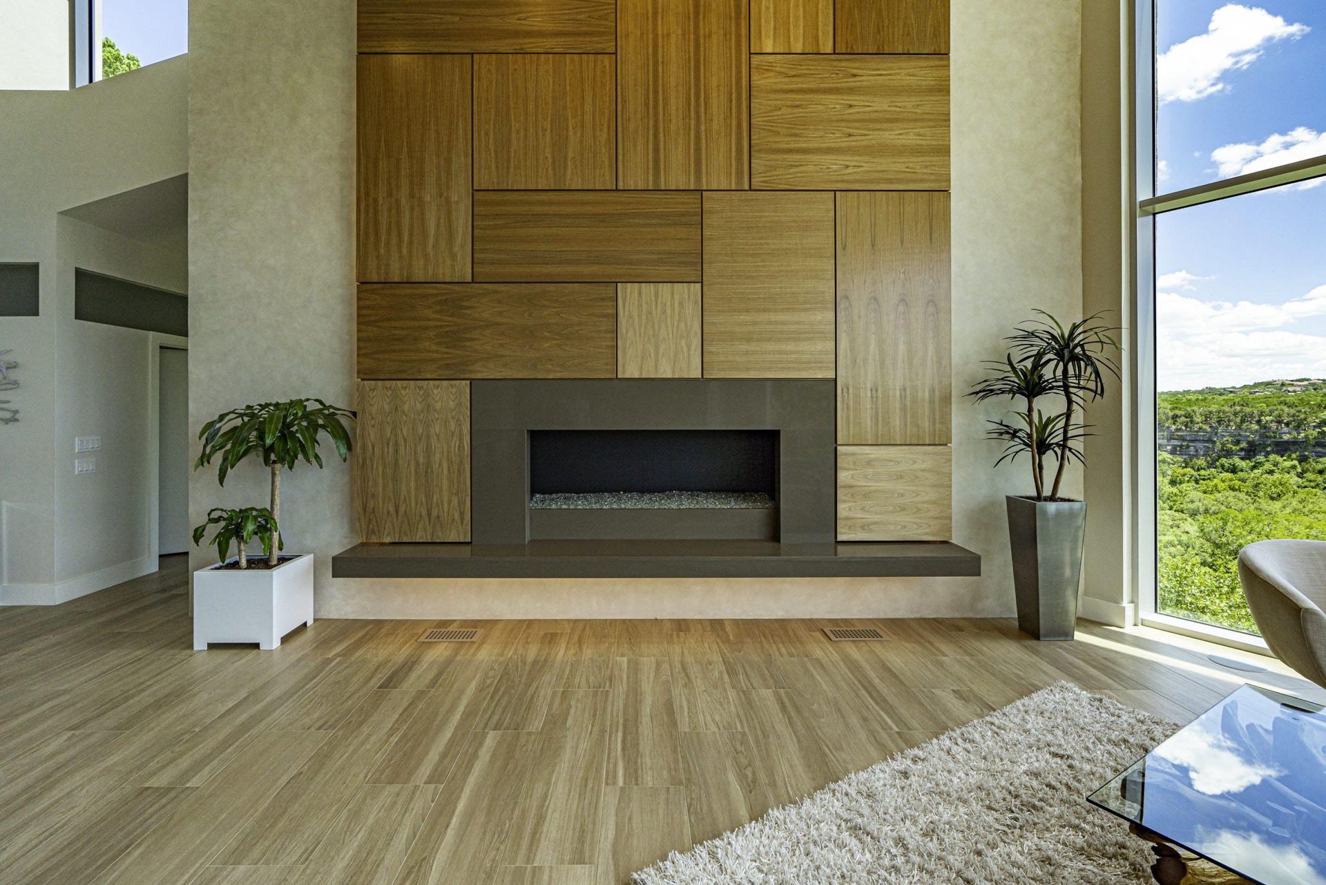 Modern living room with a wood-paneled fireplace, large window with a view, and hardwood floors.