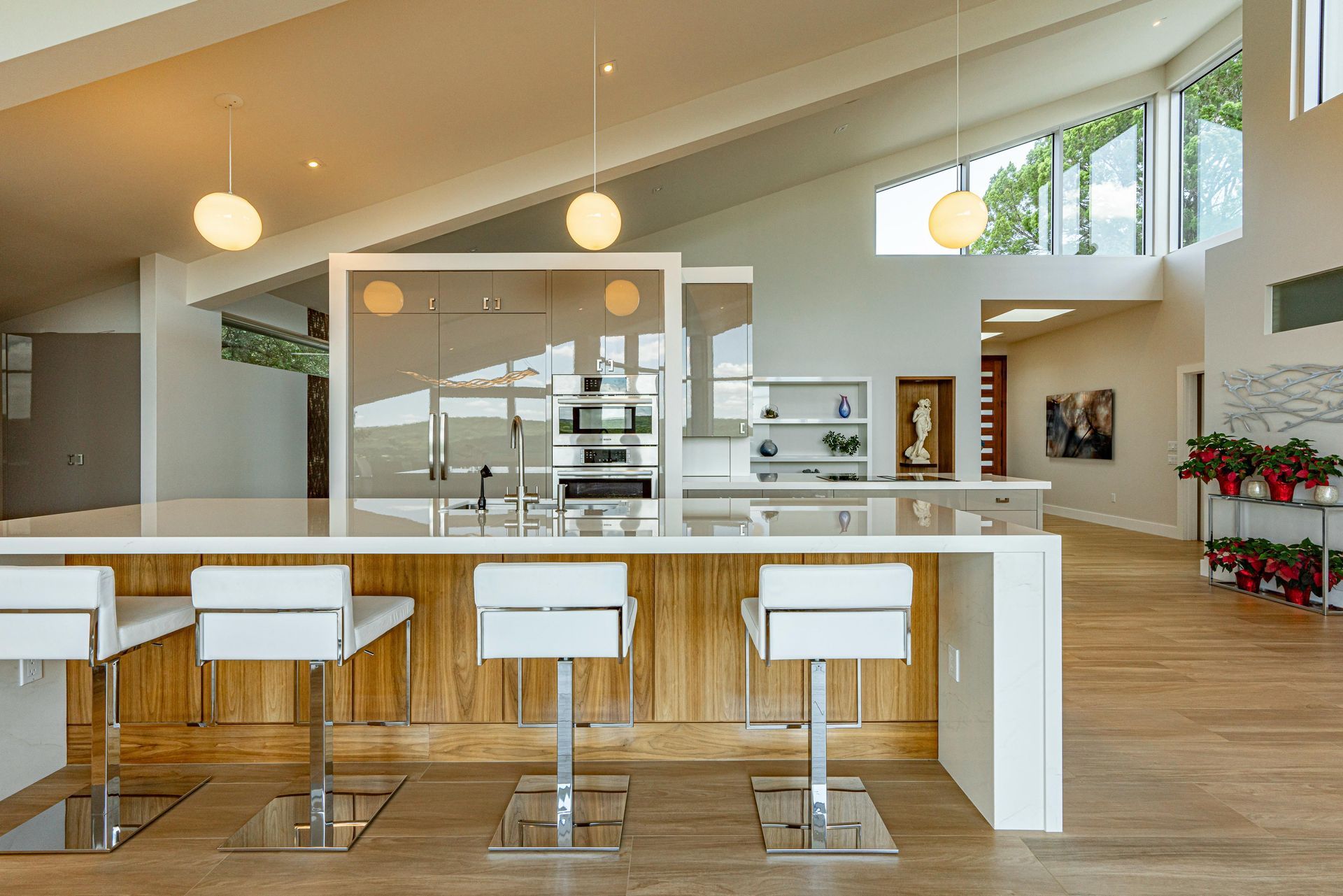 Modern kitchen with white island, stools, and wood paneling. Stainless steel appliances, bright light, and windows.