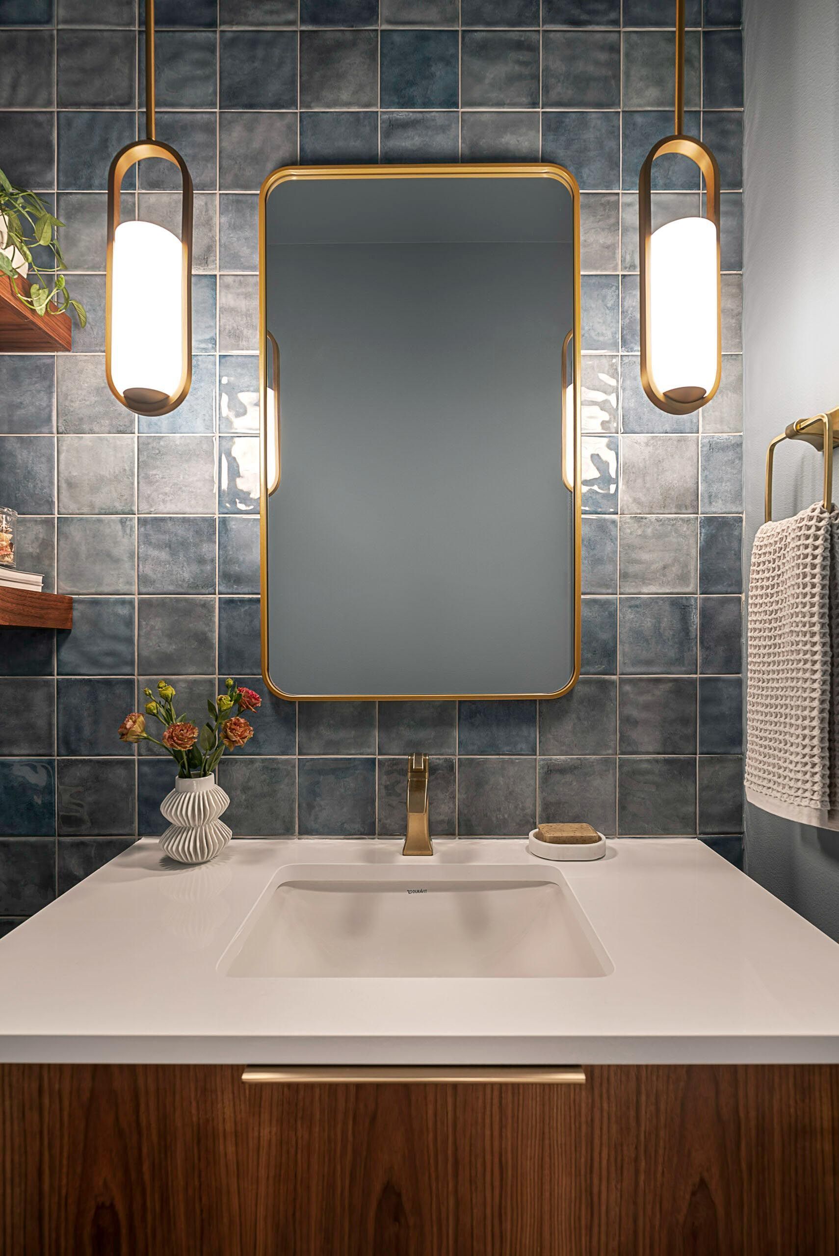 Bathroom with blue tiled wall, gold mirror, pendant lights, and wooden vanity.
