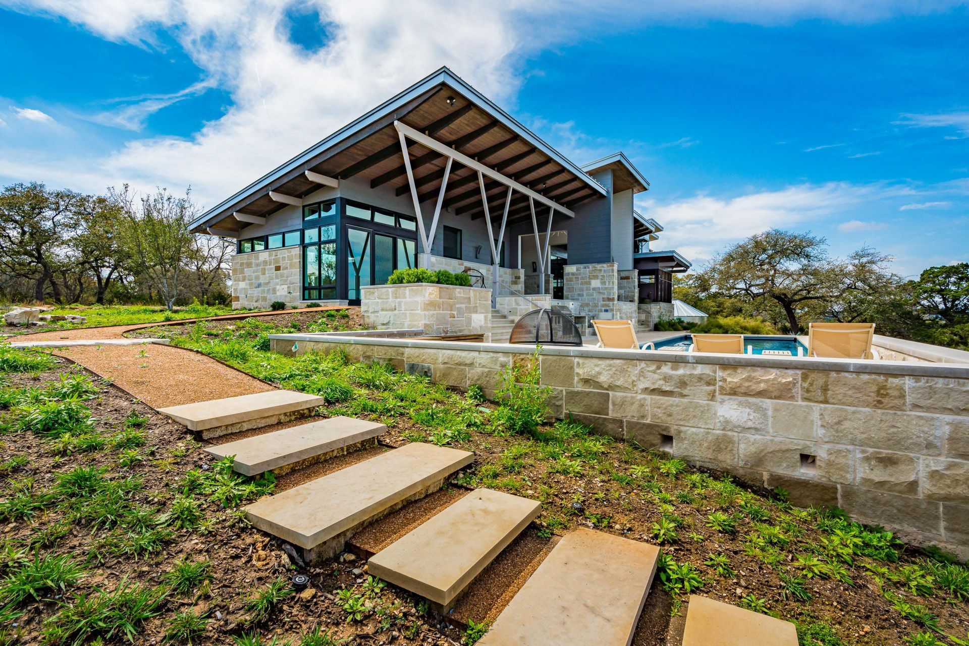 Modern house with stone and glass exterior, patio with pool, and stone path leading up to it.