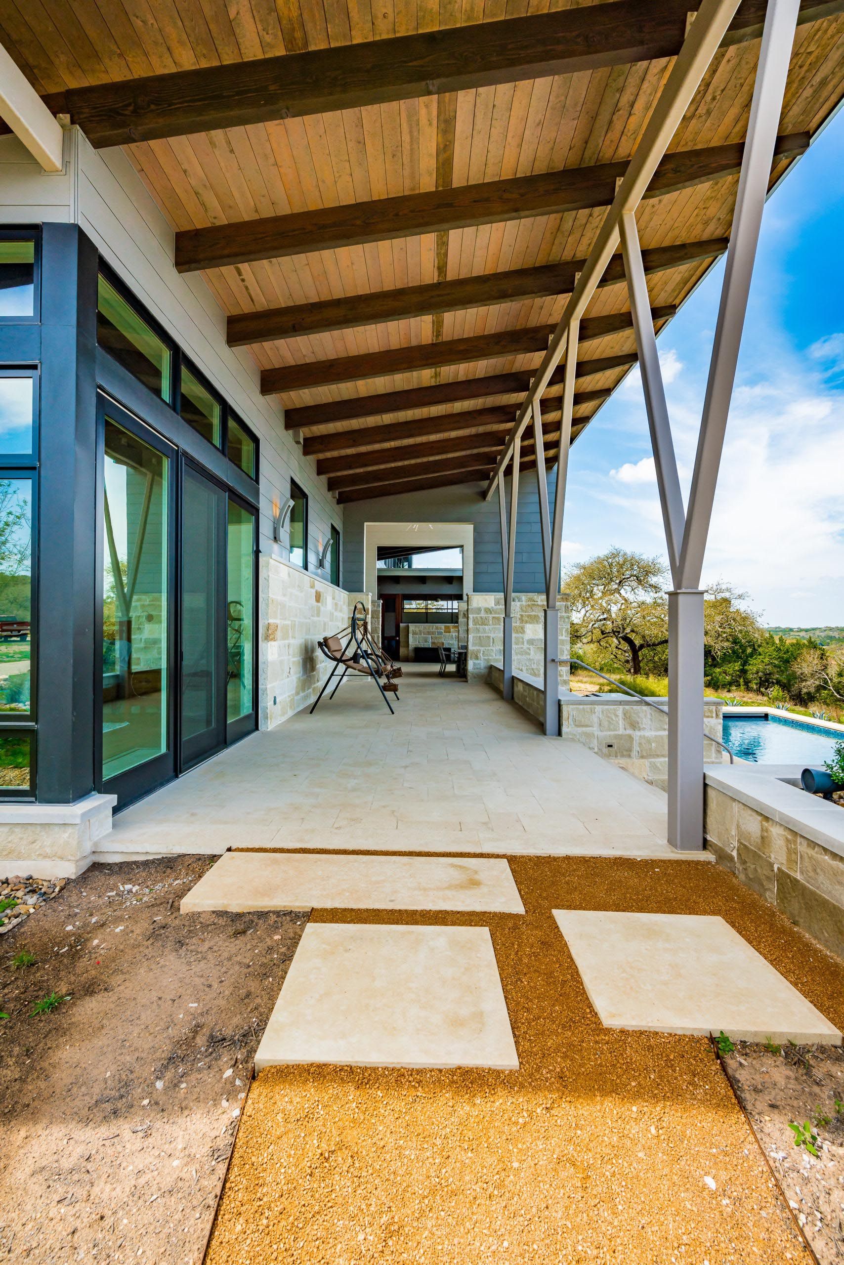 Patio with stone pavers, wooden beams, and a view of a pool.