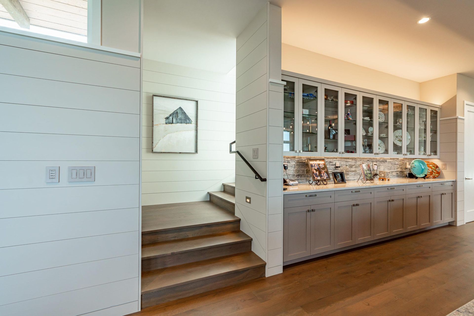 Staircase leading up, next to a built-in cabinet with glass-front display and lower cabinets.
