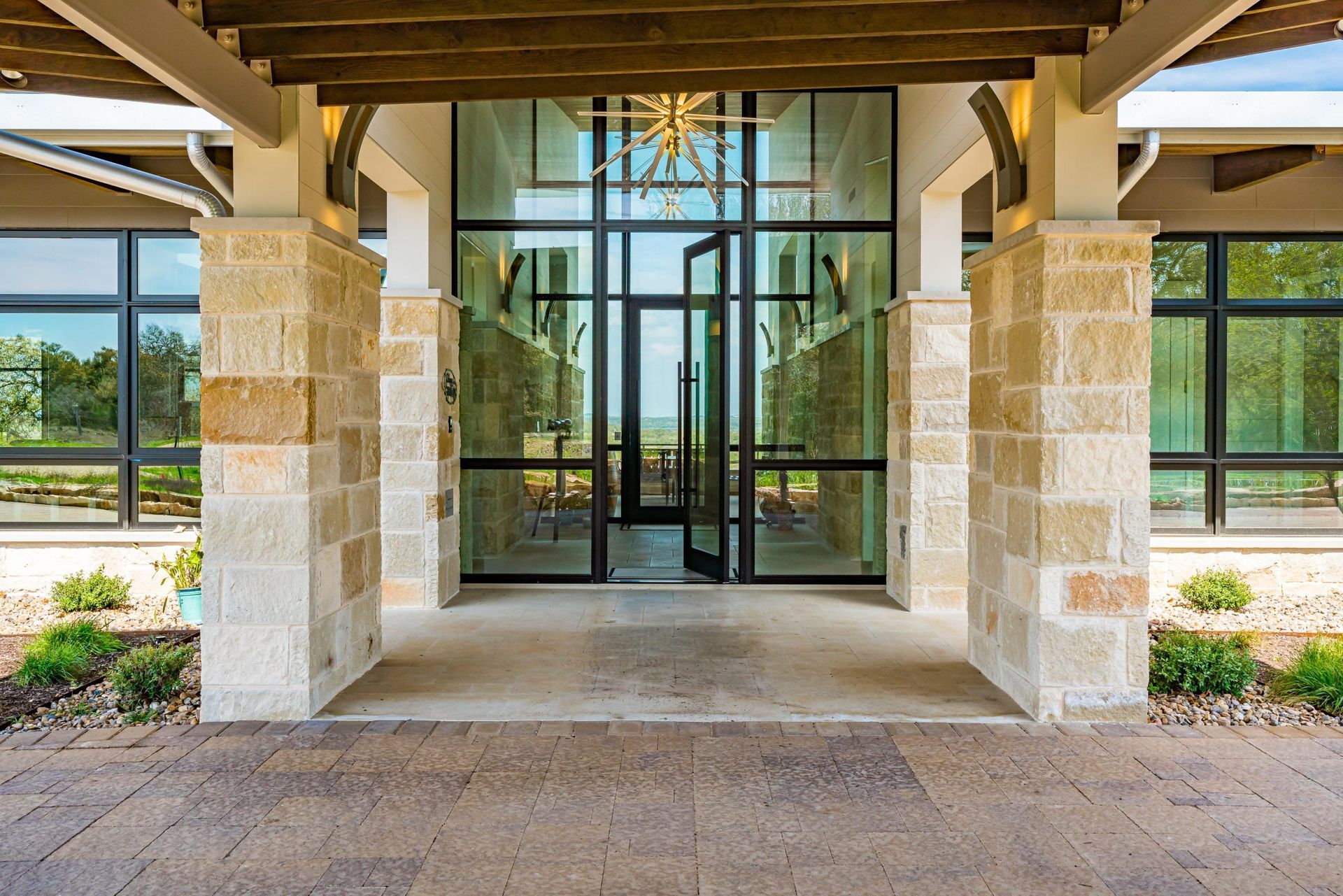 Stone columns frame glass entrance doors; building with large windows, landscaping.