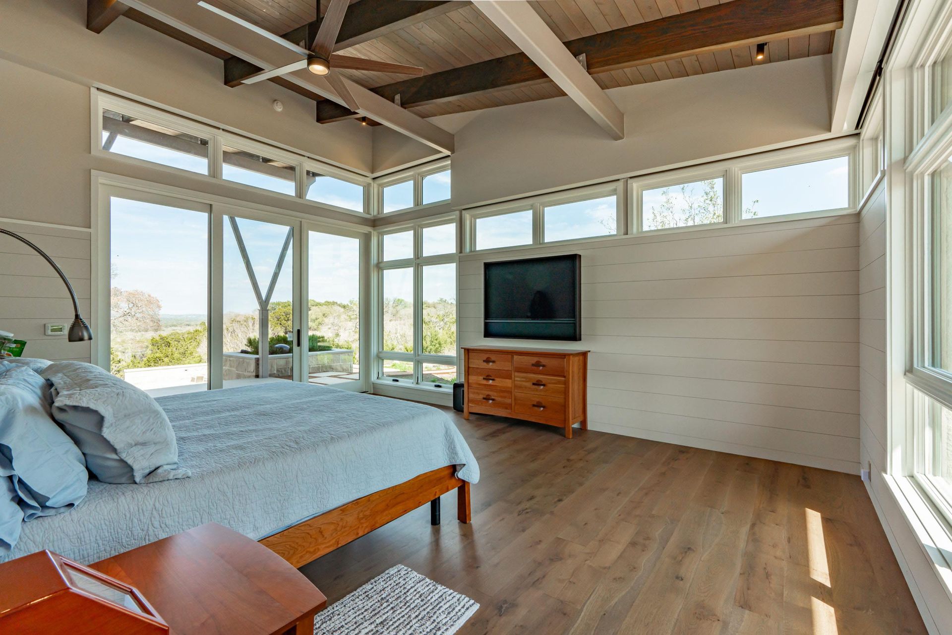 Bedroom with large windows, wood floors, bed, dresser, and TV.