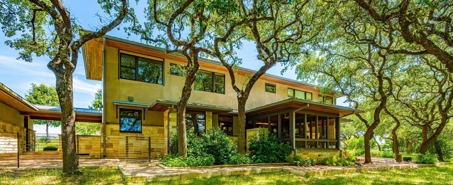 Beige two-story house with a screened porch under green trees on a sunny day.