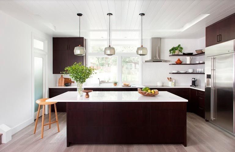 Modern kitchen with dark cabinetry, white countertops, and three pendant lights.