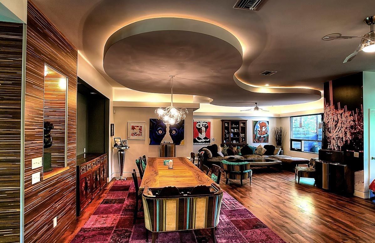Dining room with wood floor, large table, ornate ceiling, art, and patterned wall.