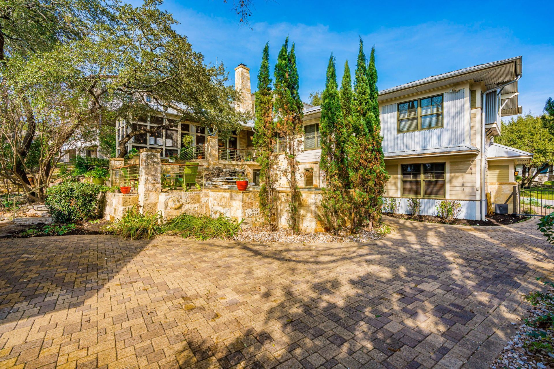 Large house with stone facade, trees, and brick driveway on a sunny day.