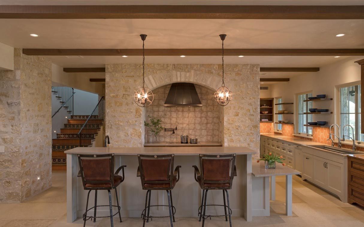 Kitchen with stone walls, island bar with stools, arched stove area, and wooden beams.