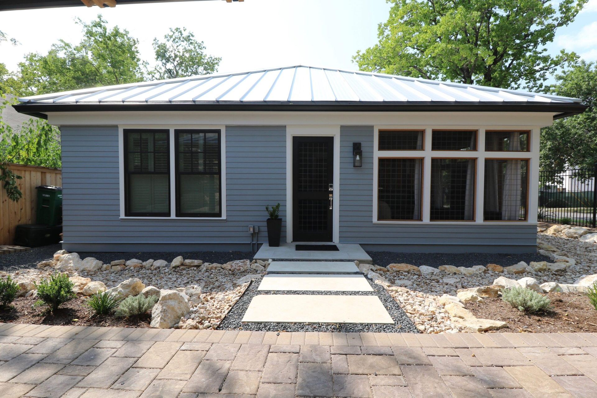 Small blue house with a white roof and black-framed windows, surrounded by rocks and a stone path.