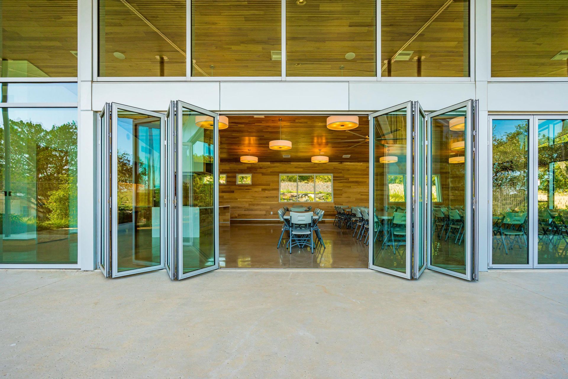 Open folding glass doors lead into a room with a table and chairs, visible from outside.