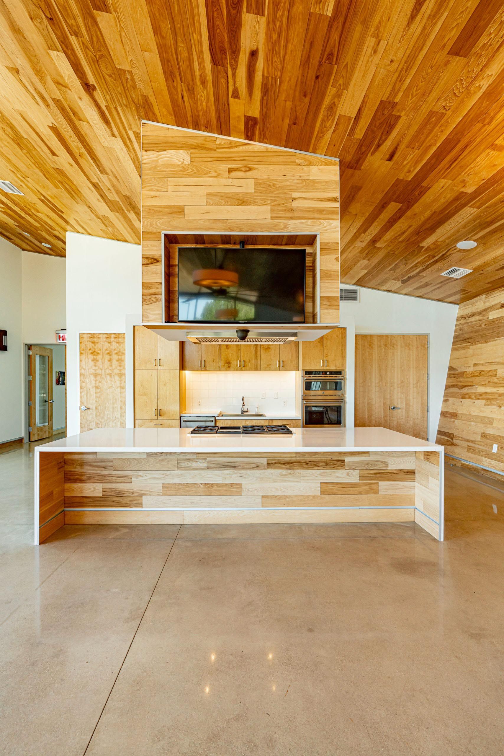 Modern kitchen with wood ceiling and accent wall, island, concrete floor, built-in appliances, and a mounted TV.