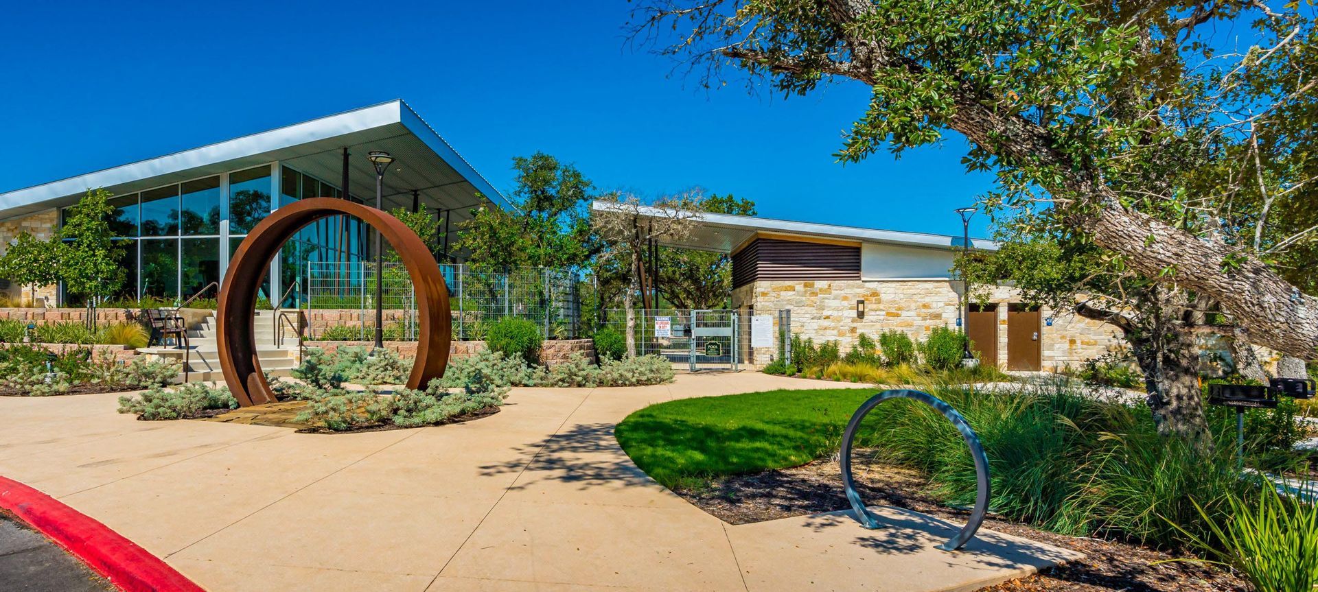 Modern building with large glass windows and metal art in a landscaped outdoor setting.