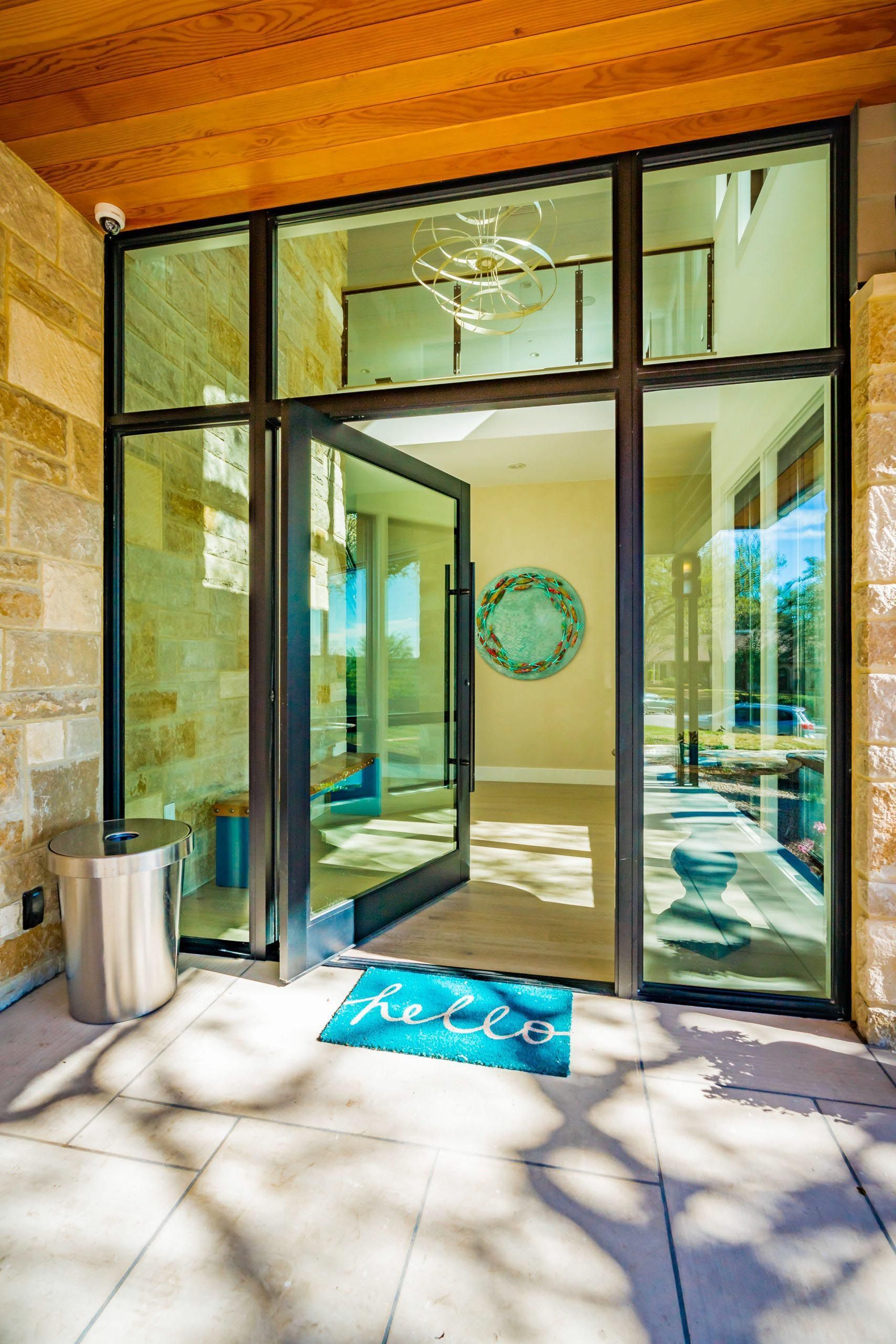 Glass front door with open door, hello doormat, and light-colored walls.
