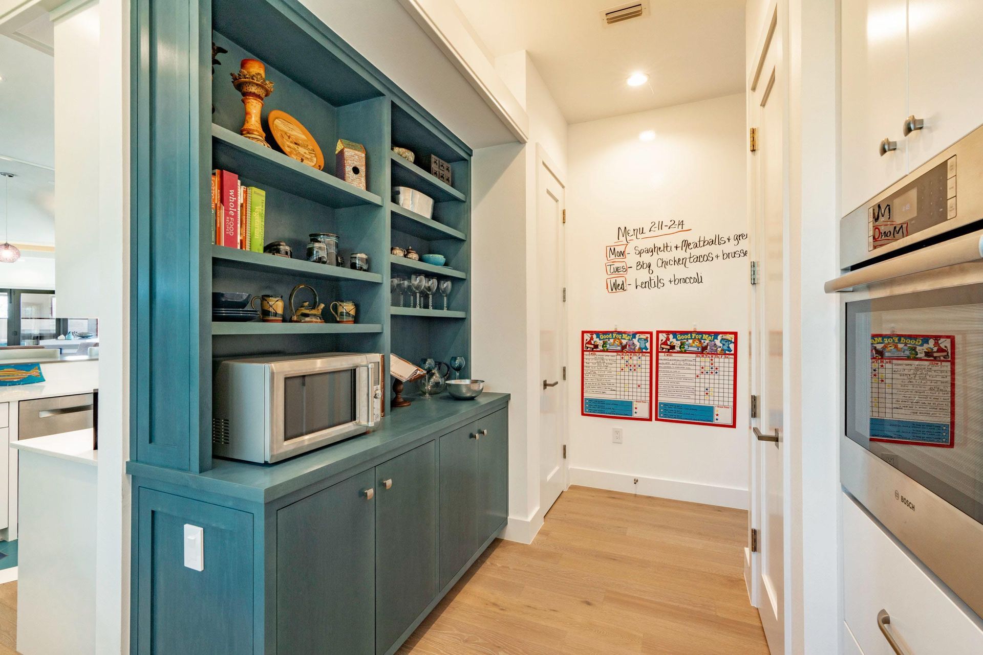 Blue built-in cabinet with microwave, shelves, and storage. Hallway with whiteboard and oven.