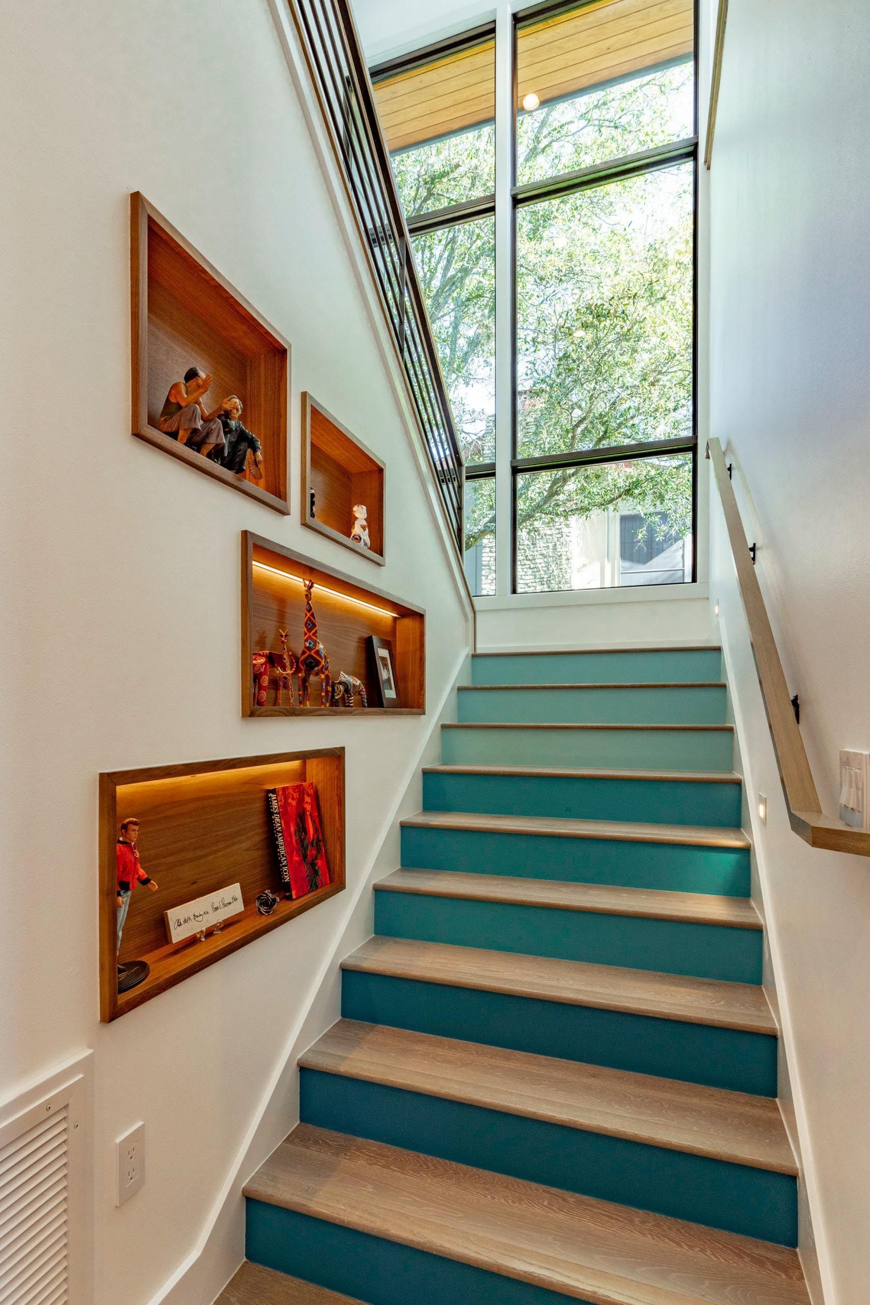 Staircase with teal blue risers, wood-framed display shelves with items, and tall window.
