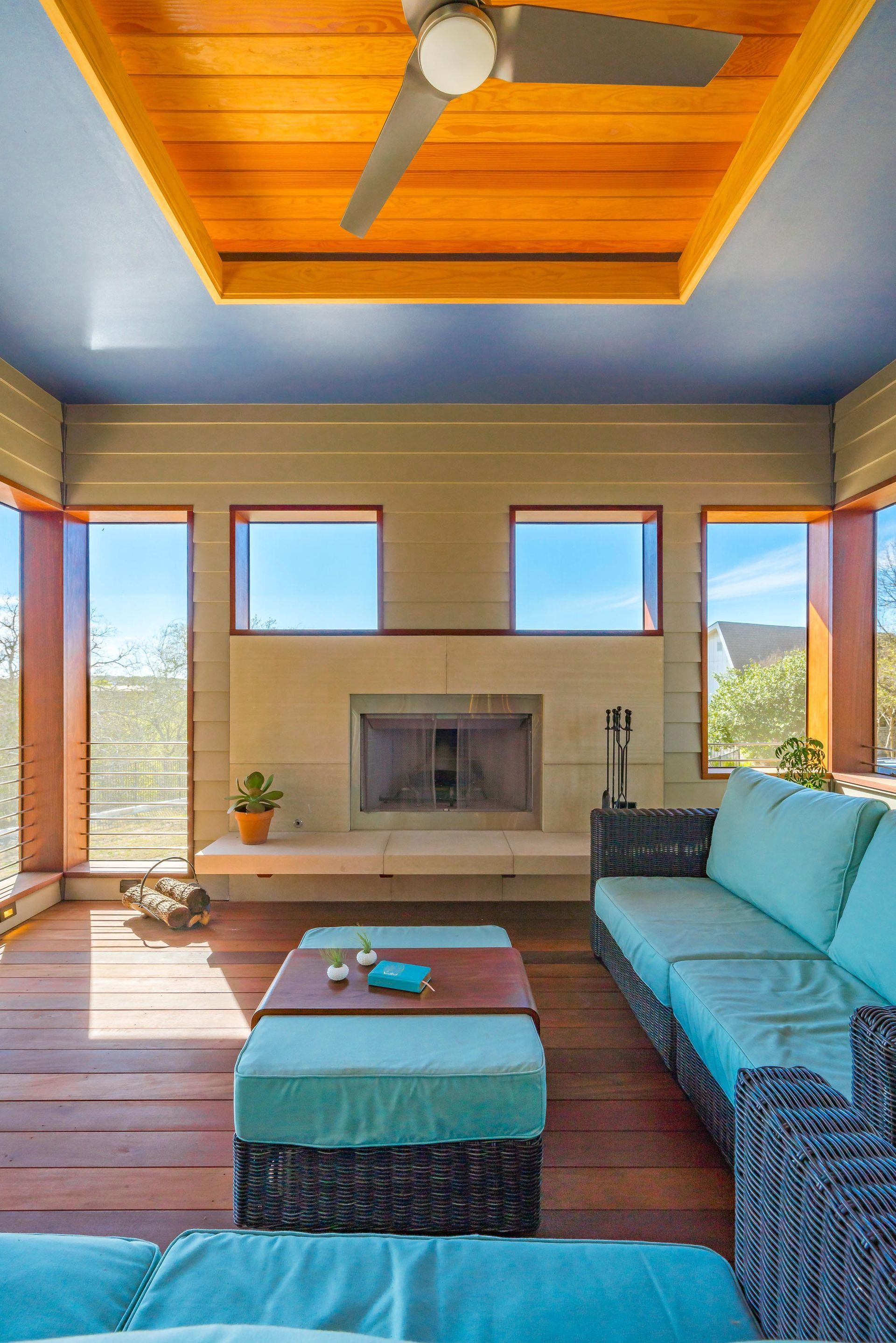 Sunroom with blue ceiling, wooden floors, fireplace, and turquoise furniture.