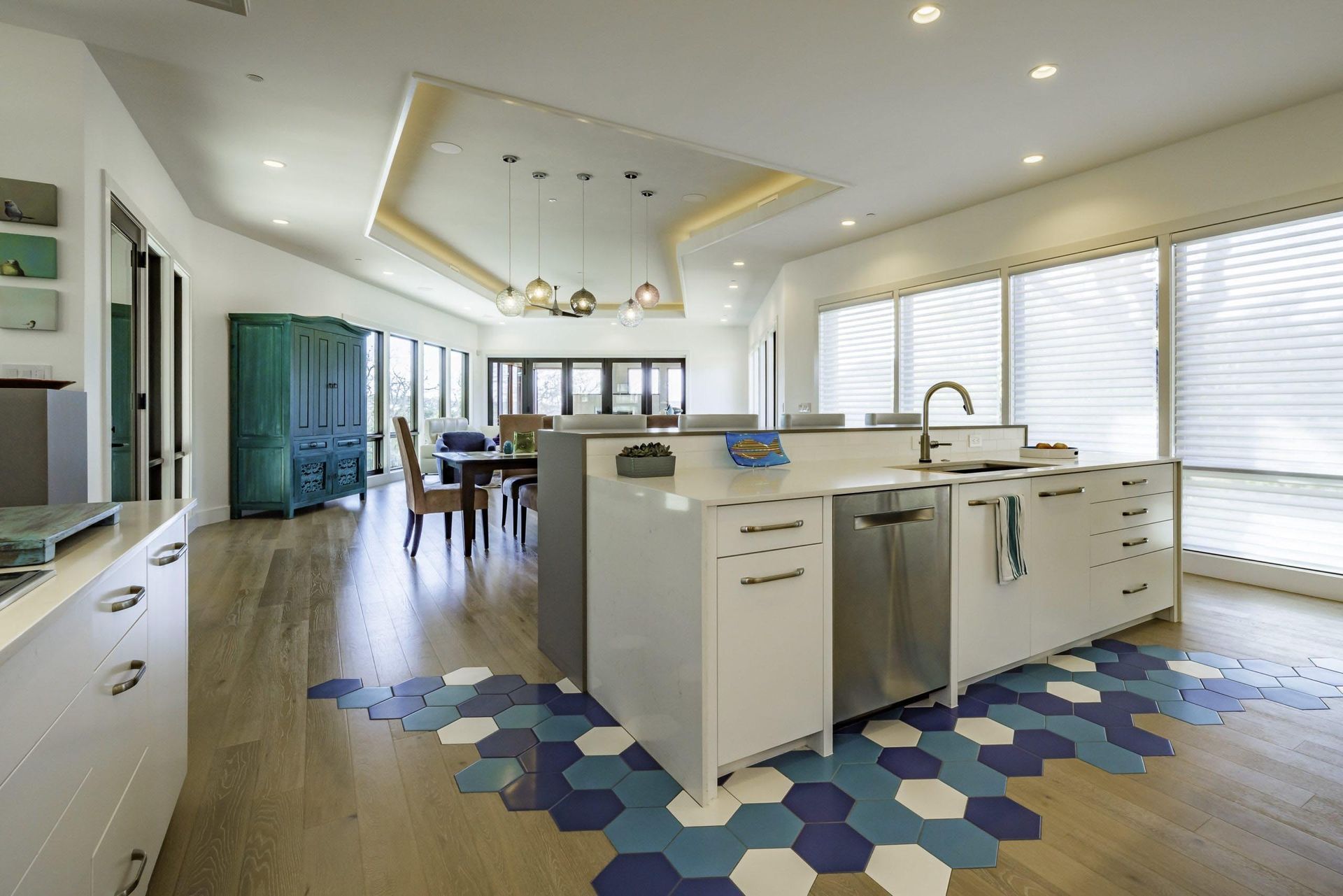 Modern kitchen with white cabinets, island with sink, and hexagonal blue tile floor.