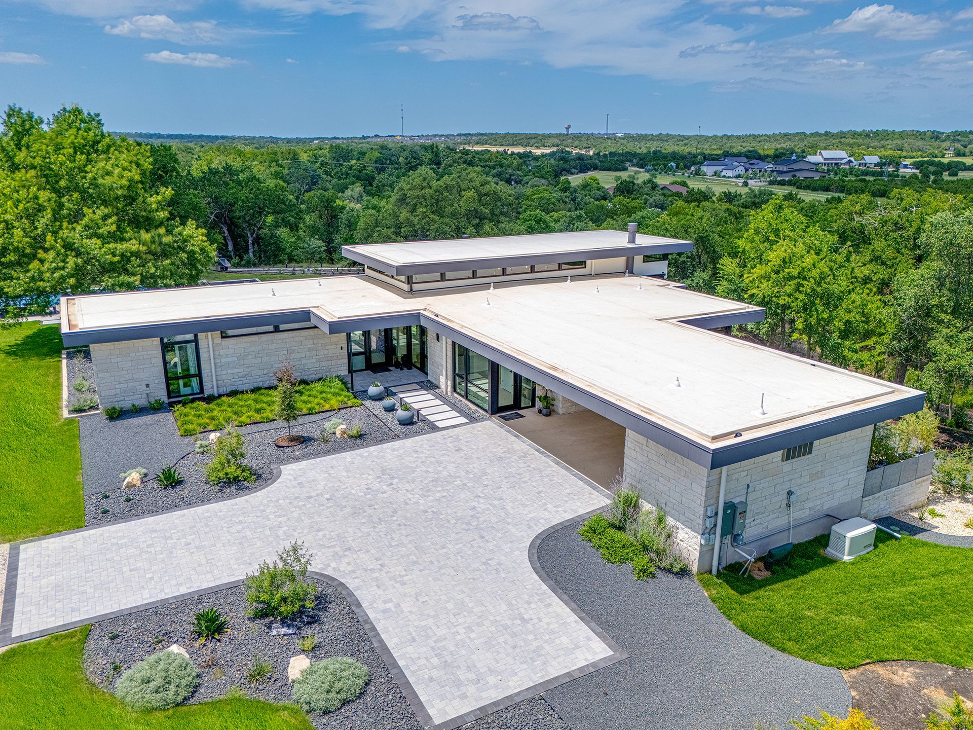 Modern home with flat roof and a long driveway, surrounded by greenery.