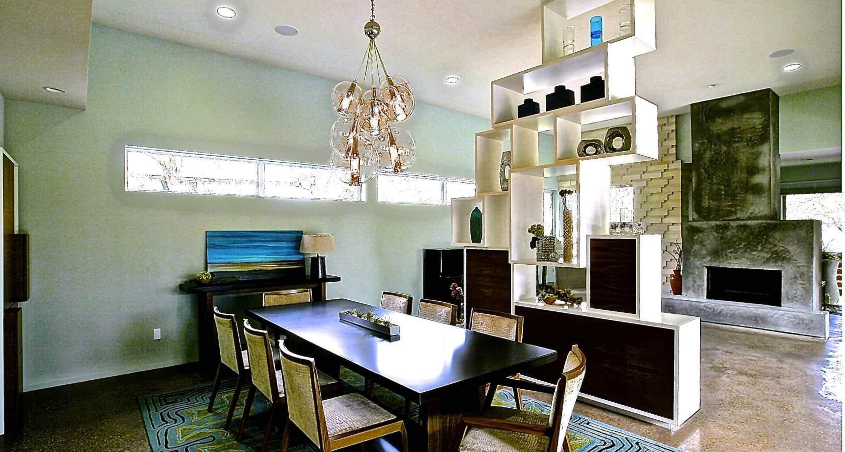 Dining room with modern chandelier, long table, display shelves, and fireplace.