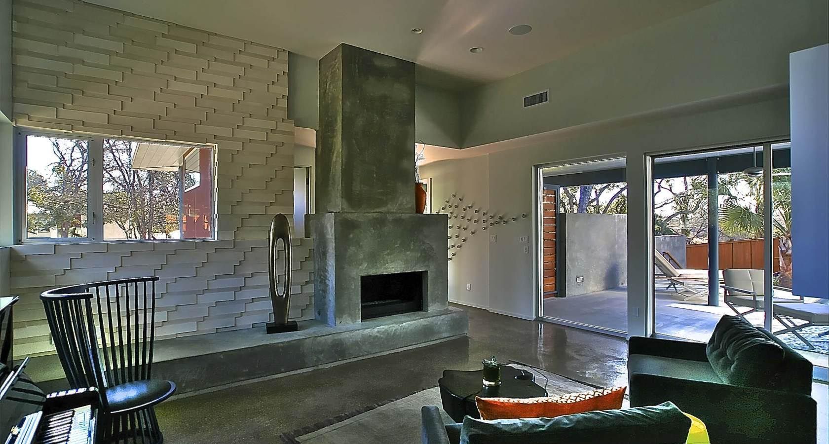 Modern living room with a concrete fireplace, light-colored brick wall, and large windows.