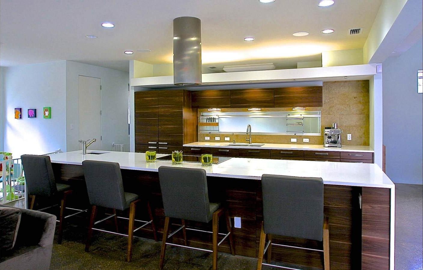 Modern kitchen with a long white countertop and gray bar stools, wood cabinets, and a silver range hood.