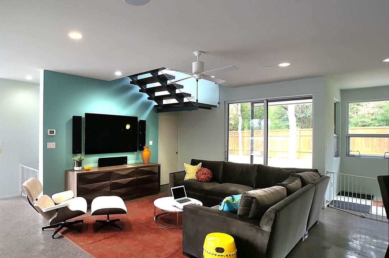 Modern living room with a teal accent wall, sectional sofa, and floating staircase.