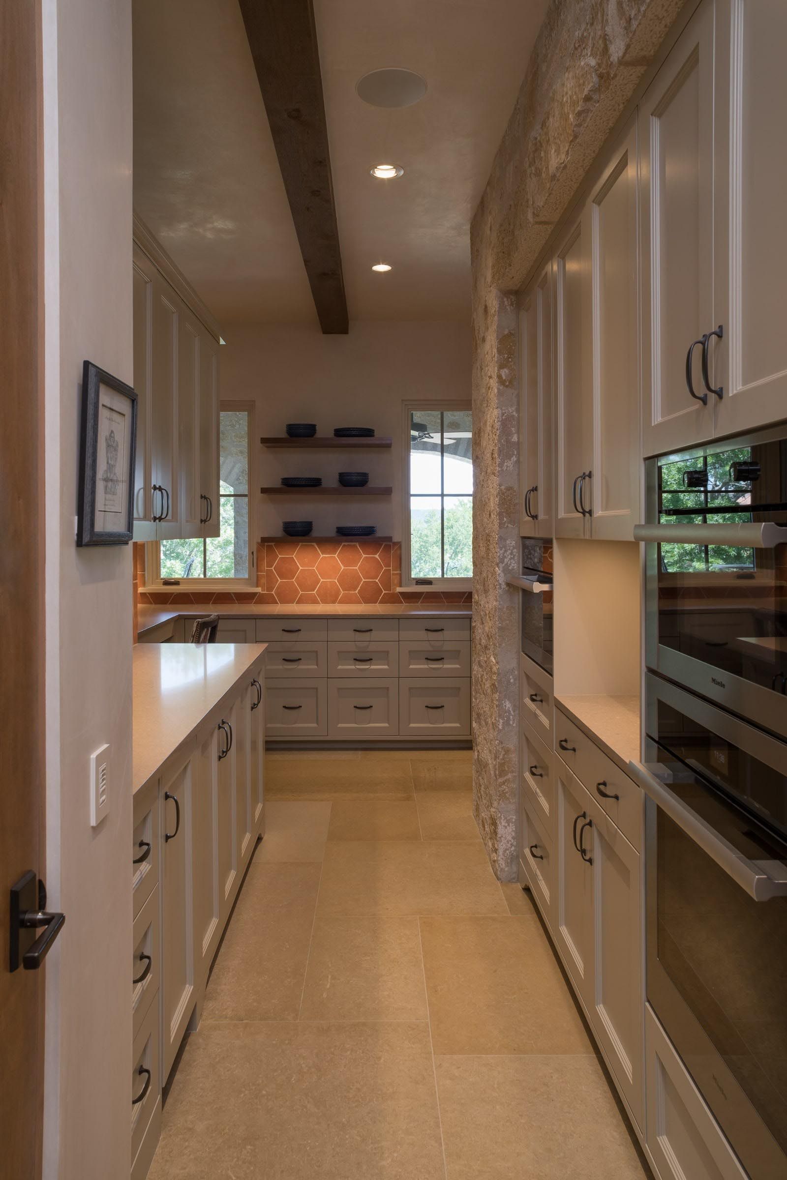 Narrow kitchen with white cabinets, stone accent wall, and wood beams on the ceiling.