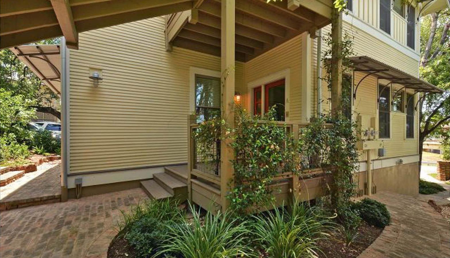 Yellow house exterior with a small porch, green foliage, and brick walkway.