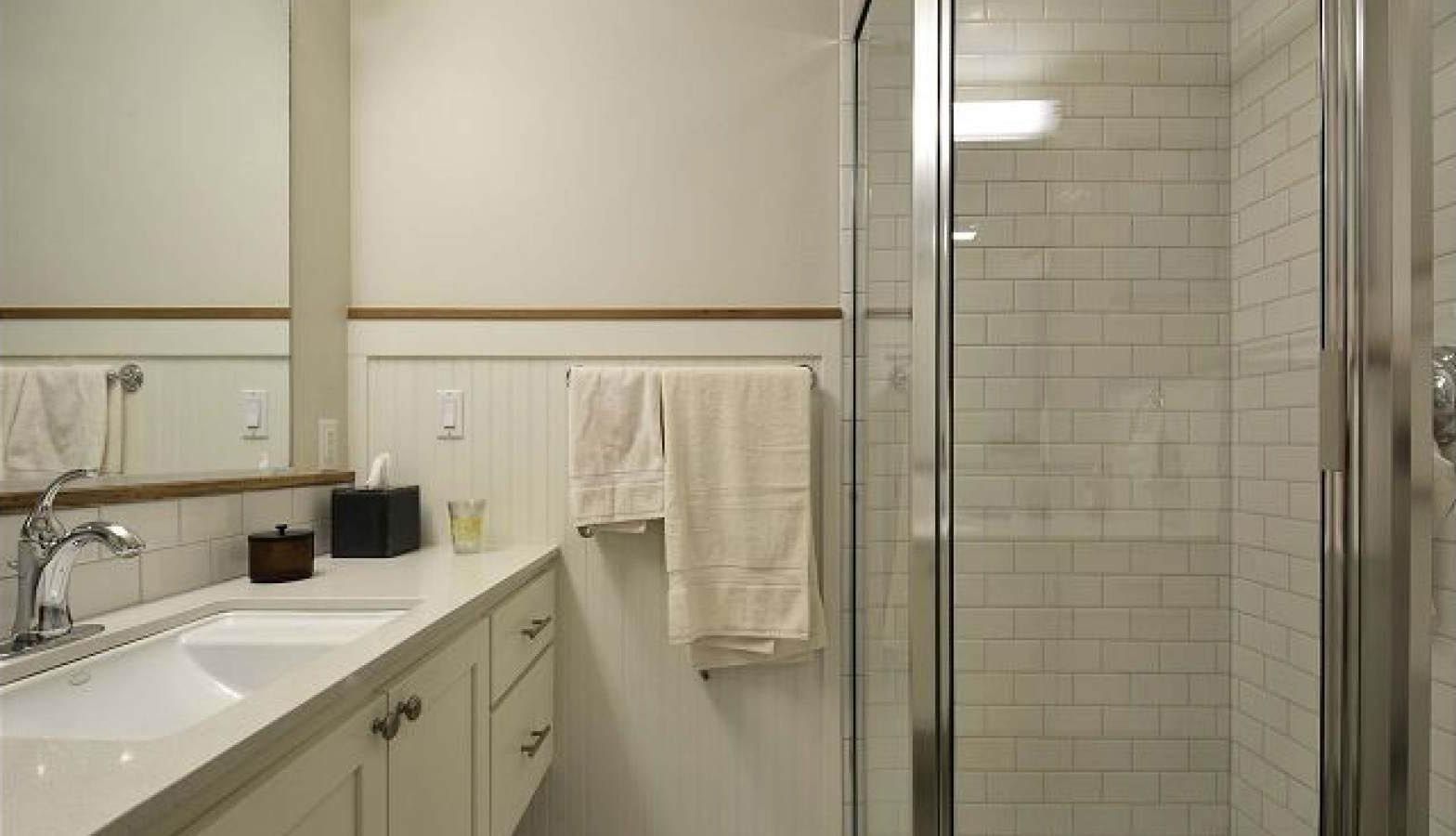 White bathroom with a shower, sink, and mirror. Beige towel hangs on a wall.
