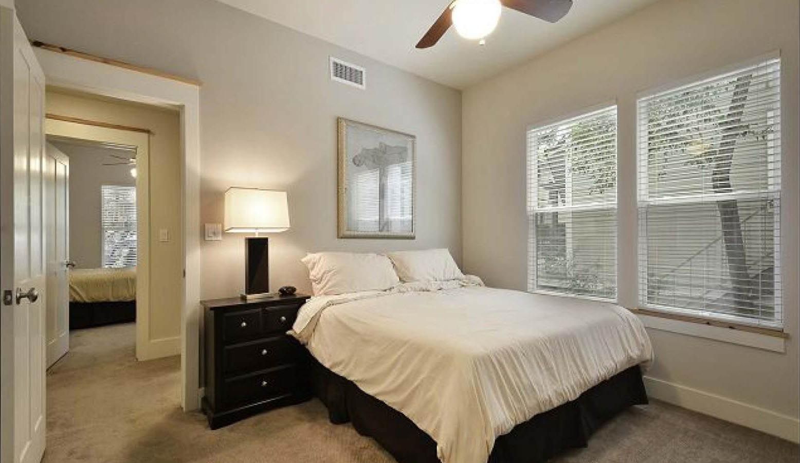 Bedroom with a bed, dresser, windows with blinds, and doorway to another room.