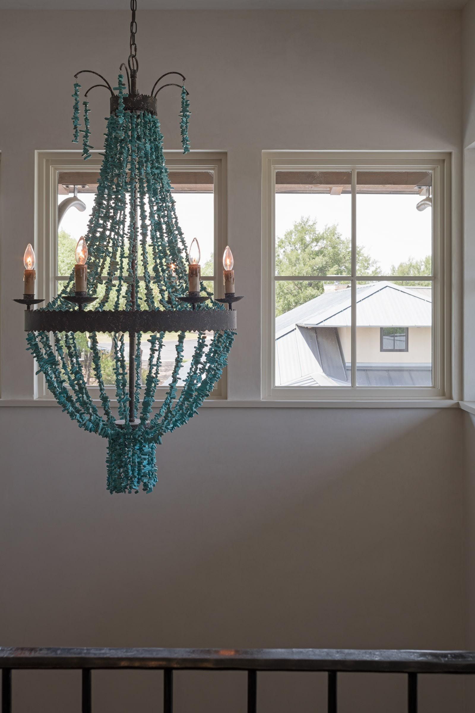 Beaded turquoise chandelier hangs in front of two windows.