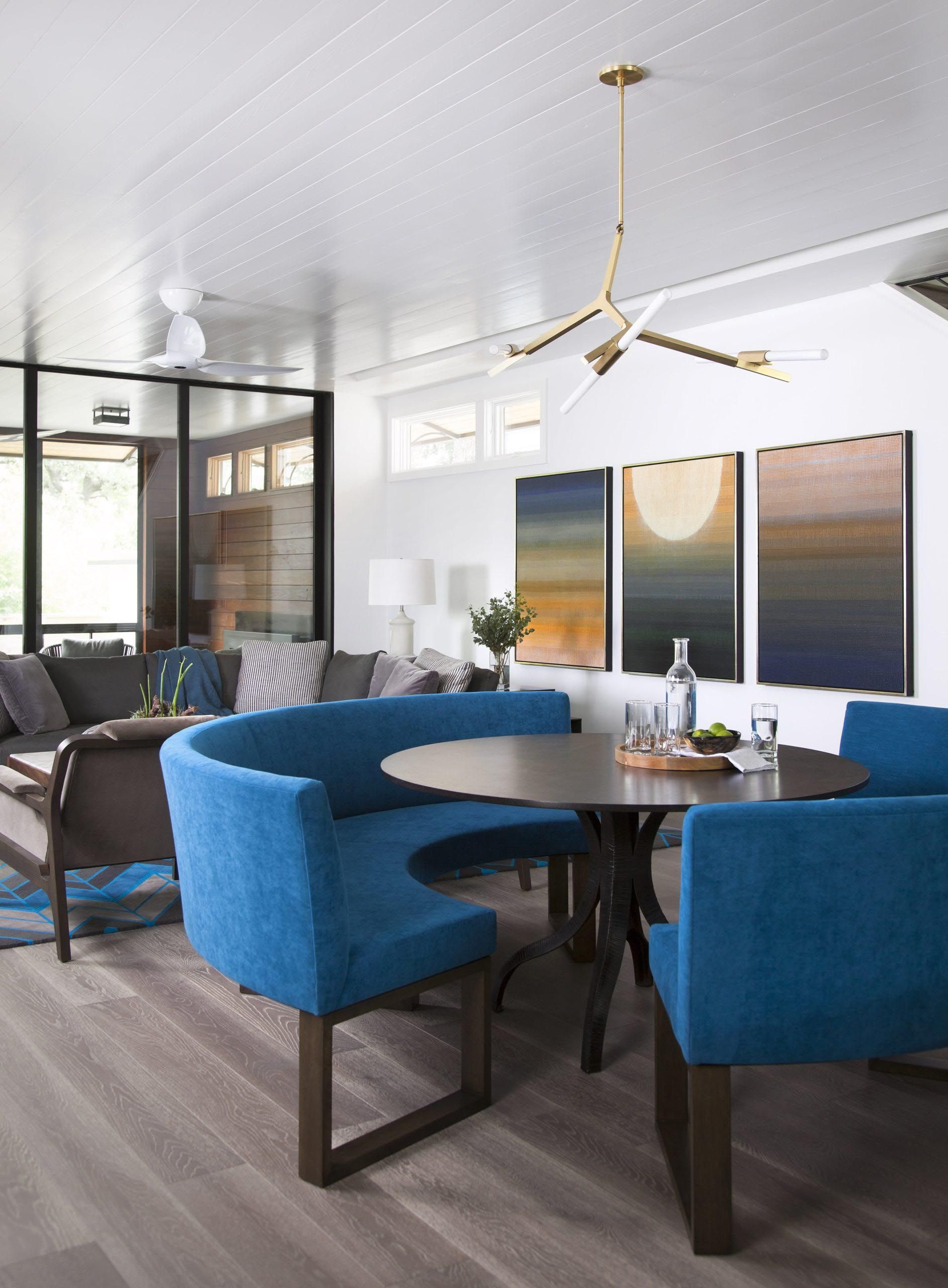 A dining area with a round table, blue booth, and chairs, with artwork and a chandelier.