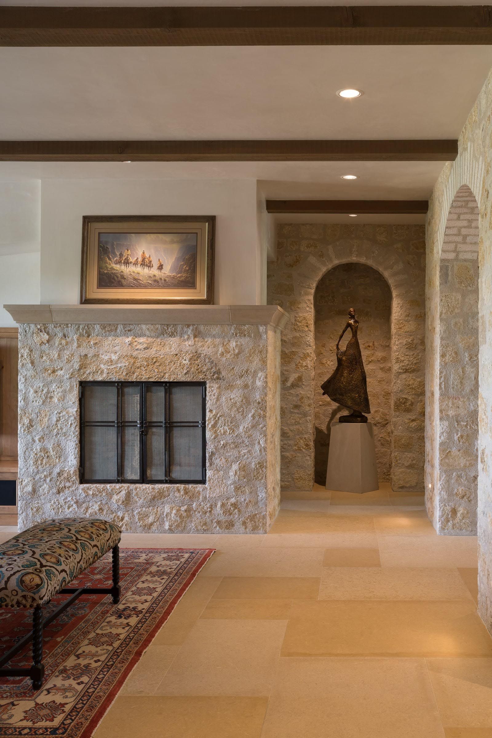 Stone fireplace with art, bench, and sculpture in an arched alcove. Beige and brown tones.