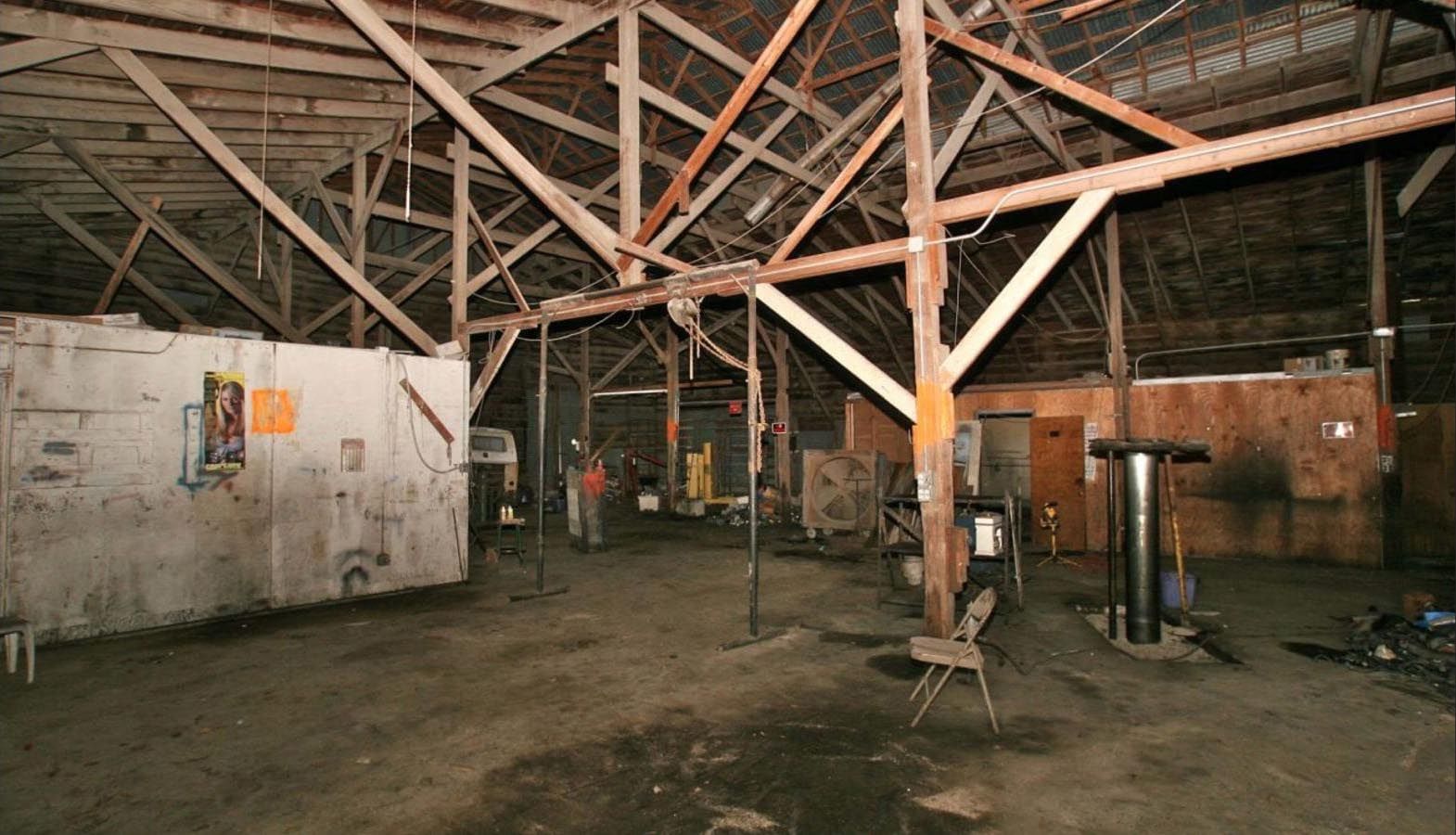 Interior of a large, dimly lit workshop with exposed wooden beams and a dirt floor.