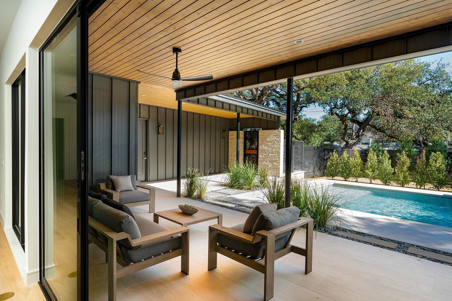 Patio with outdoor seating overlooking pool and landscaping under wooden ceiling.