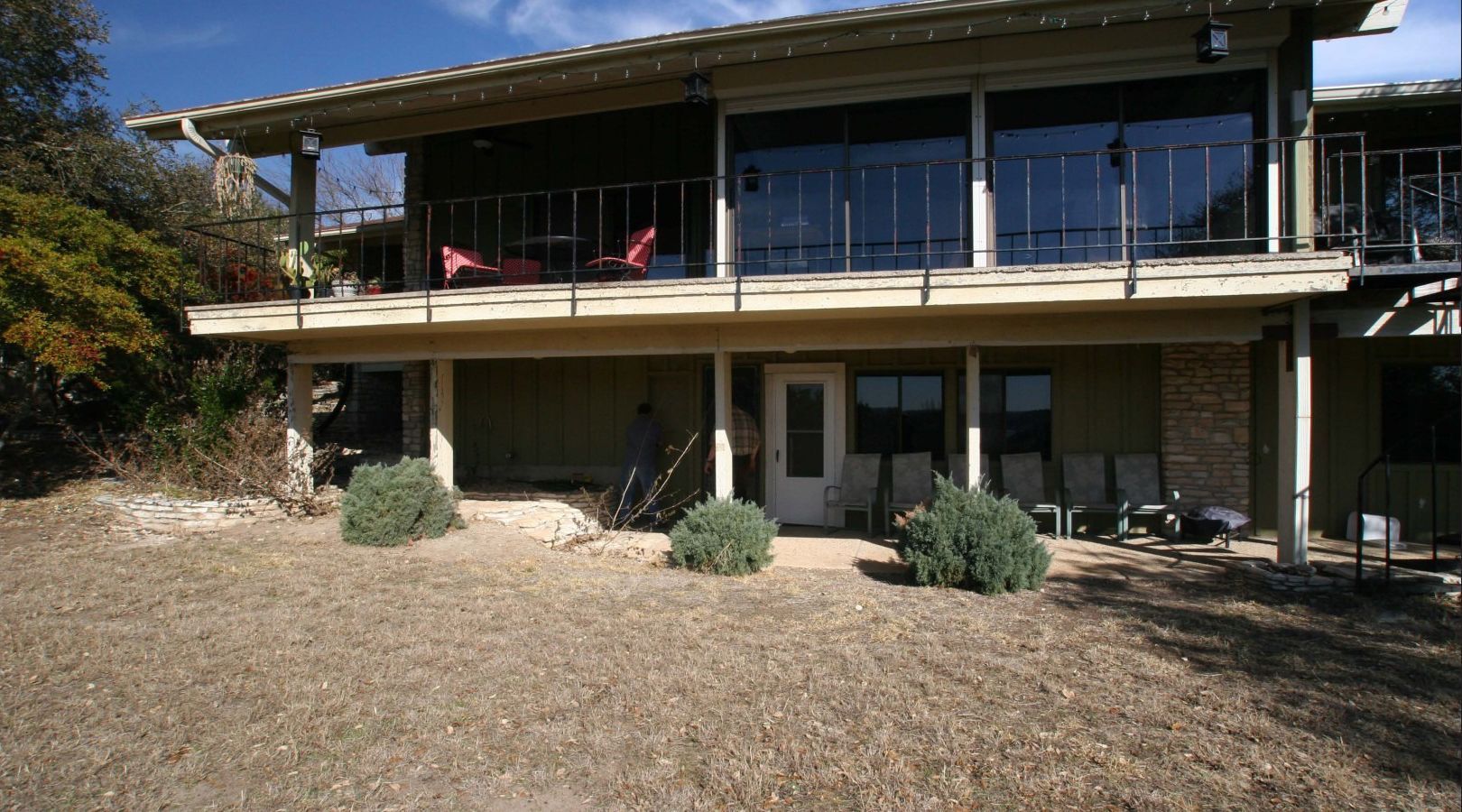 Two-story house with a wooden deck and large windows overlooking a dry, rocky yard.