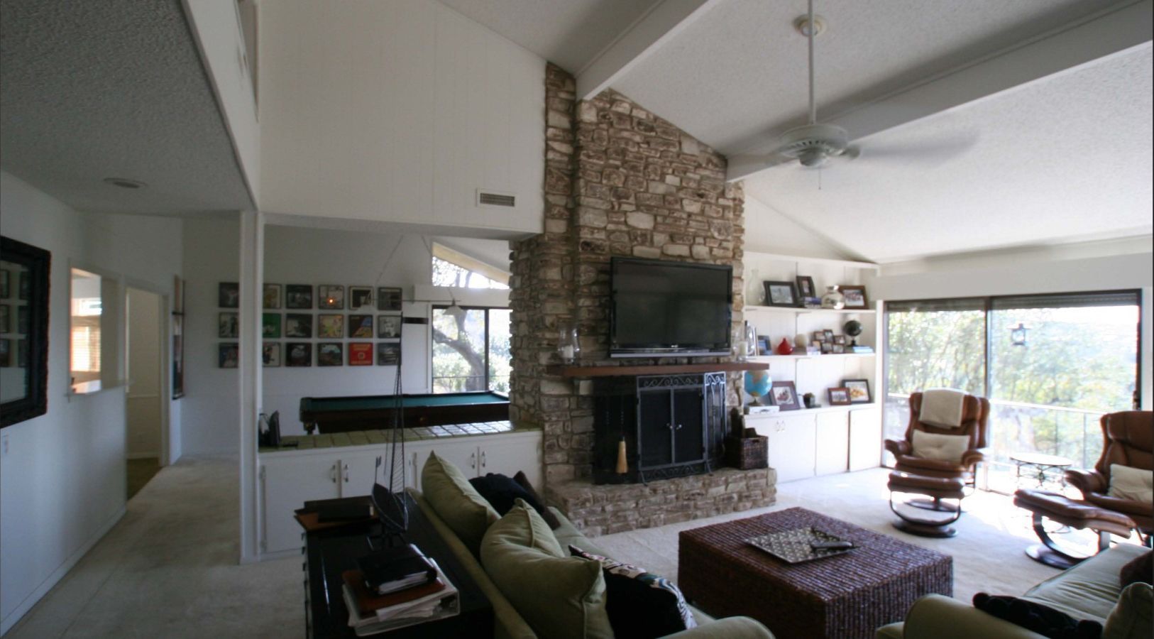 Living room with stone fireplace, TV, seating, and a pool table visible in the background.