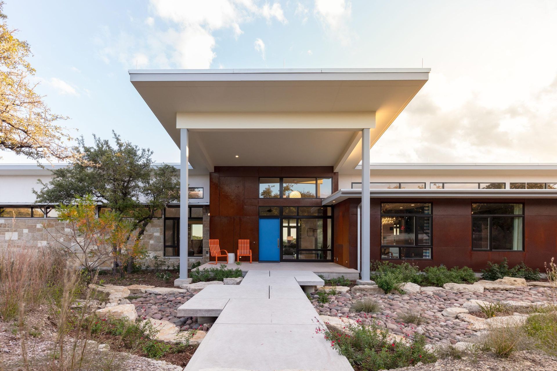 Modern home exterior with a blue door under a covered entry and concrete walkway.
