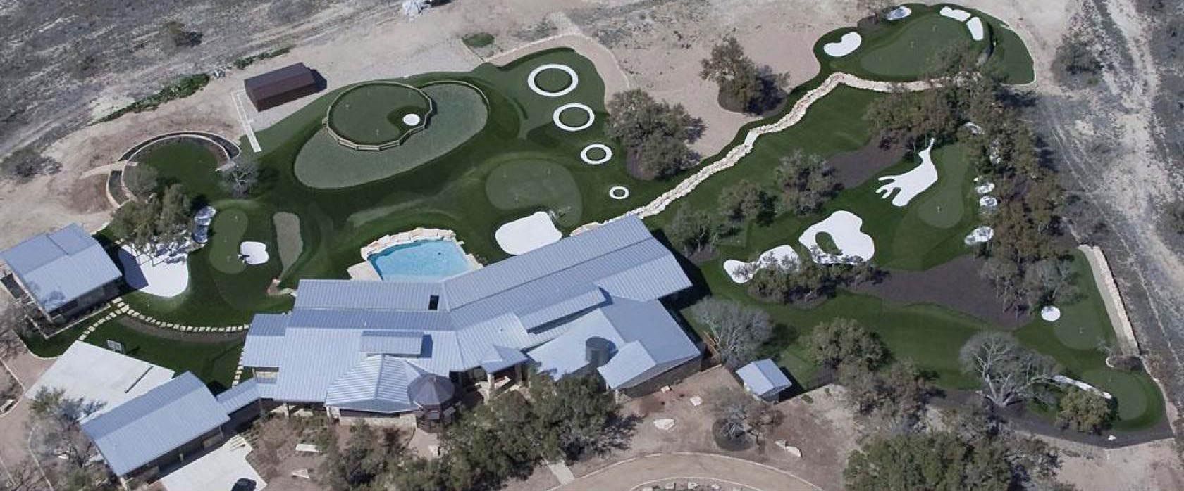 Aerial view of a large house with a golf course, pool, and multiple buildings.