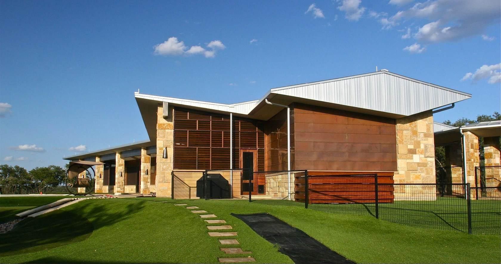 Modern building with stone and wood exterior, angled metal roof, green lawn, blue sky.