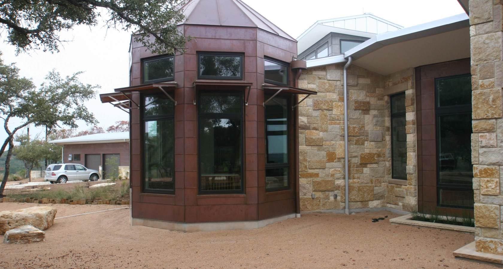Copper-clad, multi-windowed turret on a stone house with a curved roof. Car parked in the distance.