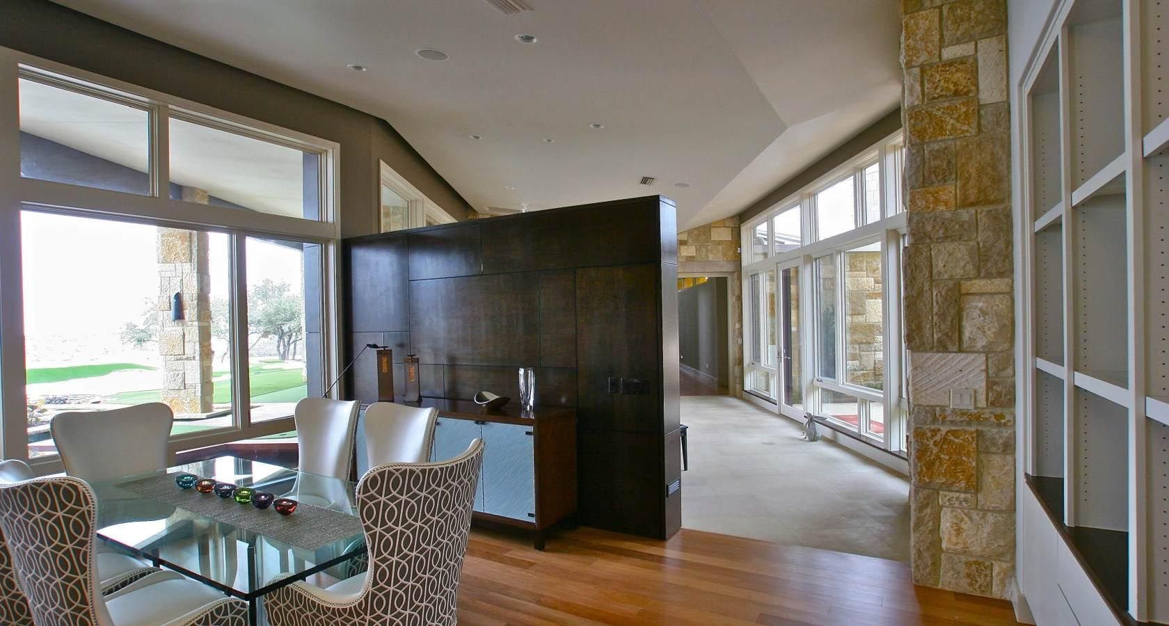 Spacious dining room with glass table, patterned chairs, dark wood cabinetry, and large windows.