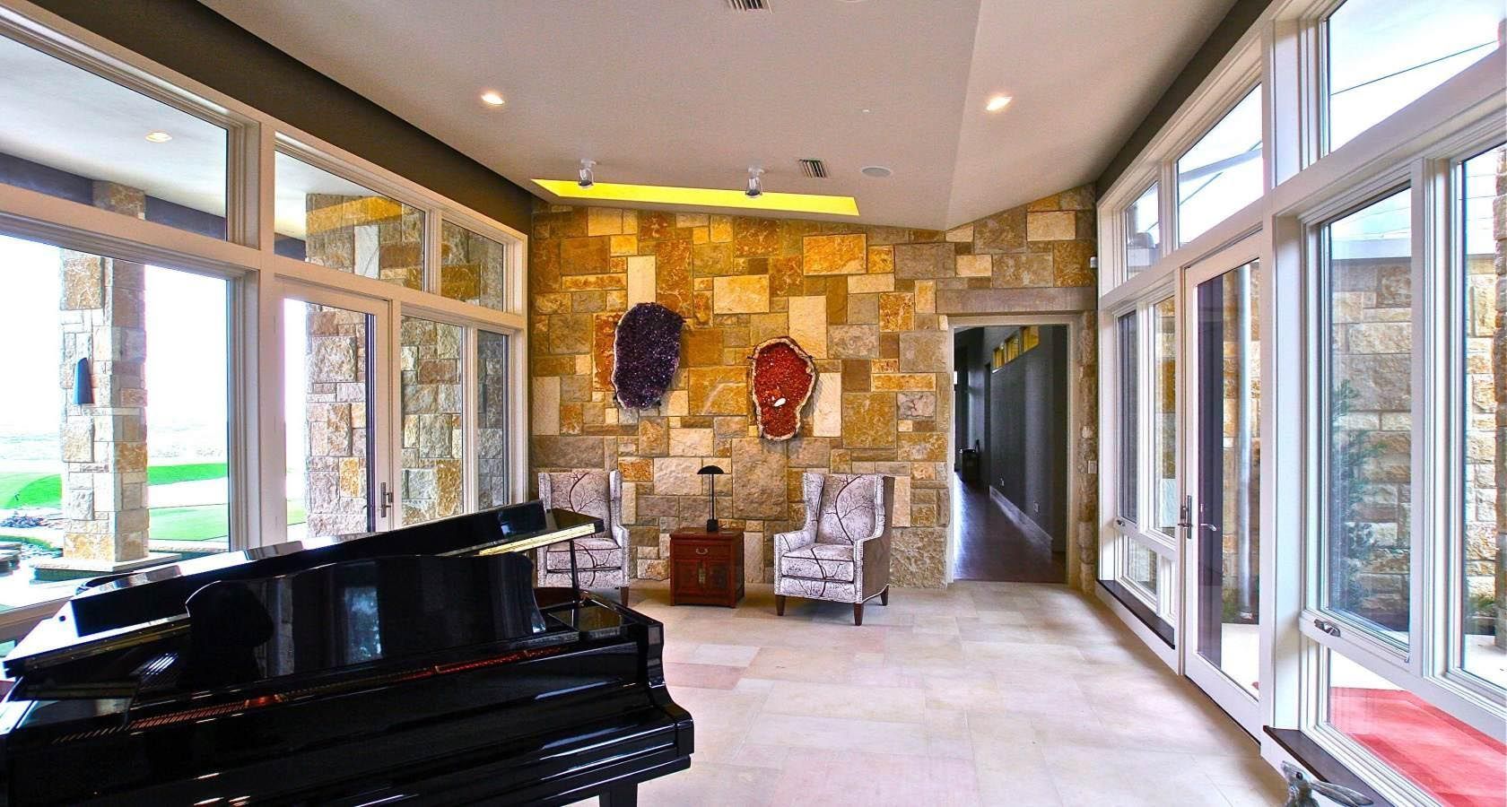 A luxury room with a grand piano, stone accent wall, and large windows overlooking a field.