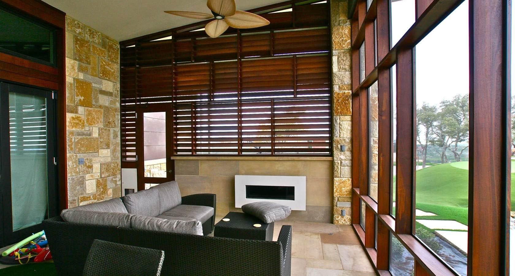Covered patio with a sofa, stone walls, and wooden blinds, overlooking a green lawn.