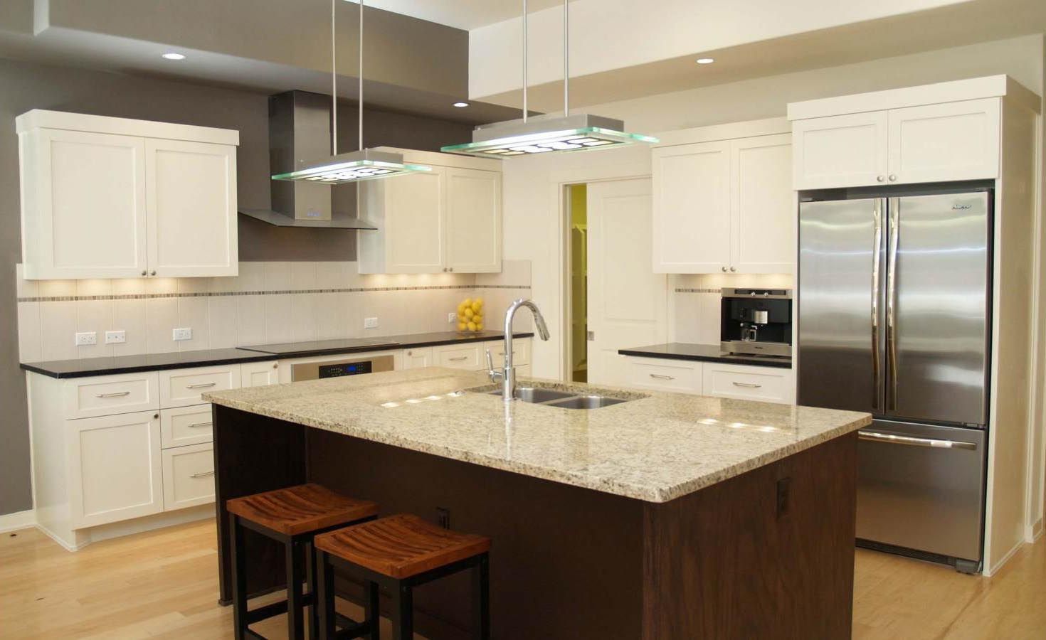 Modern white kitchen with dark wood island, stainless steel appliances, and beige granite countertops.