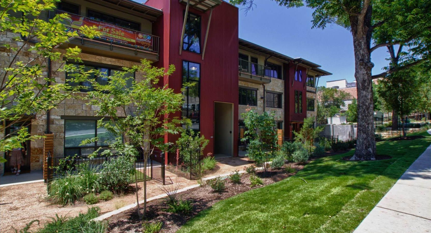 Multi-story apartment building with red and stone exterior, surrounded by trees and green lawn.