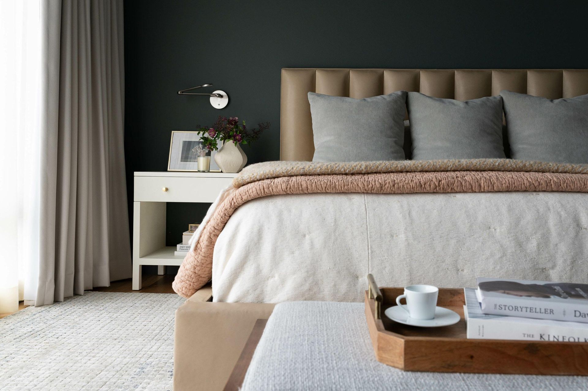 Bedroom with dark green wall, beige bed, white nightstand, gray pillows, and a wooden tray.