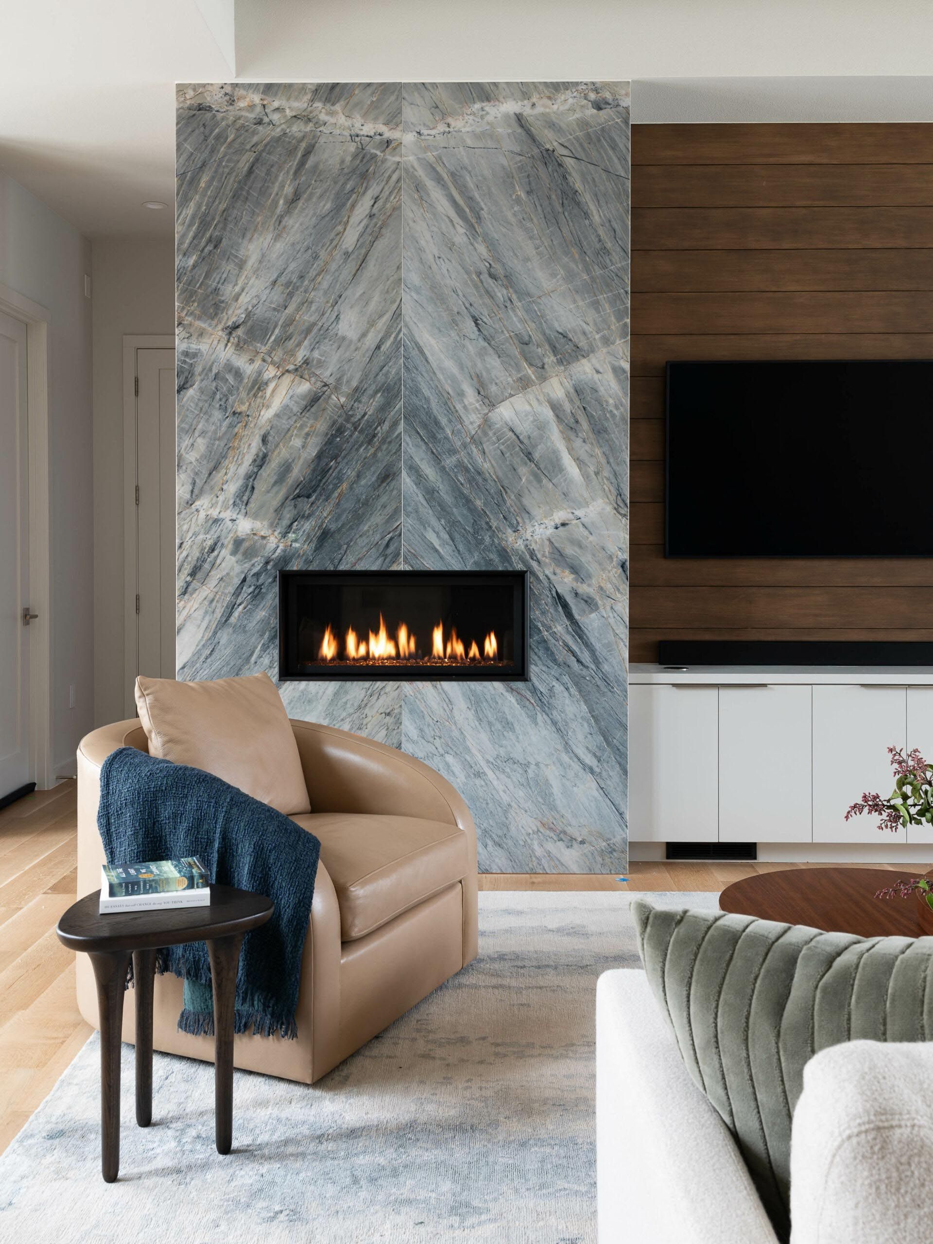Living room with a marble fireplace, leather chair, and a TV on a wood panel wall.