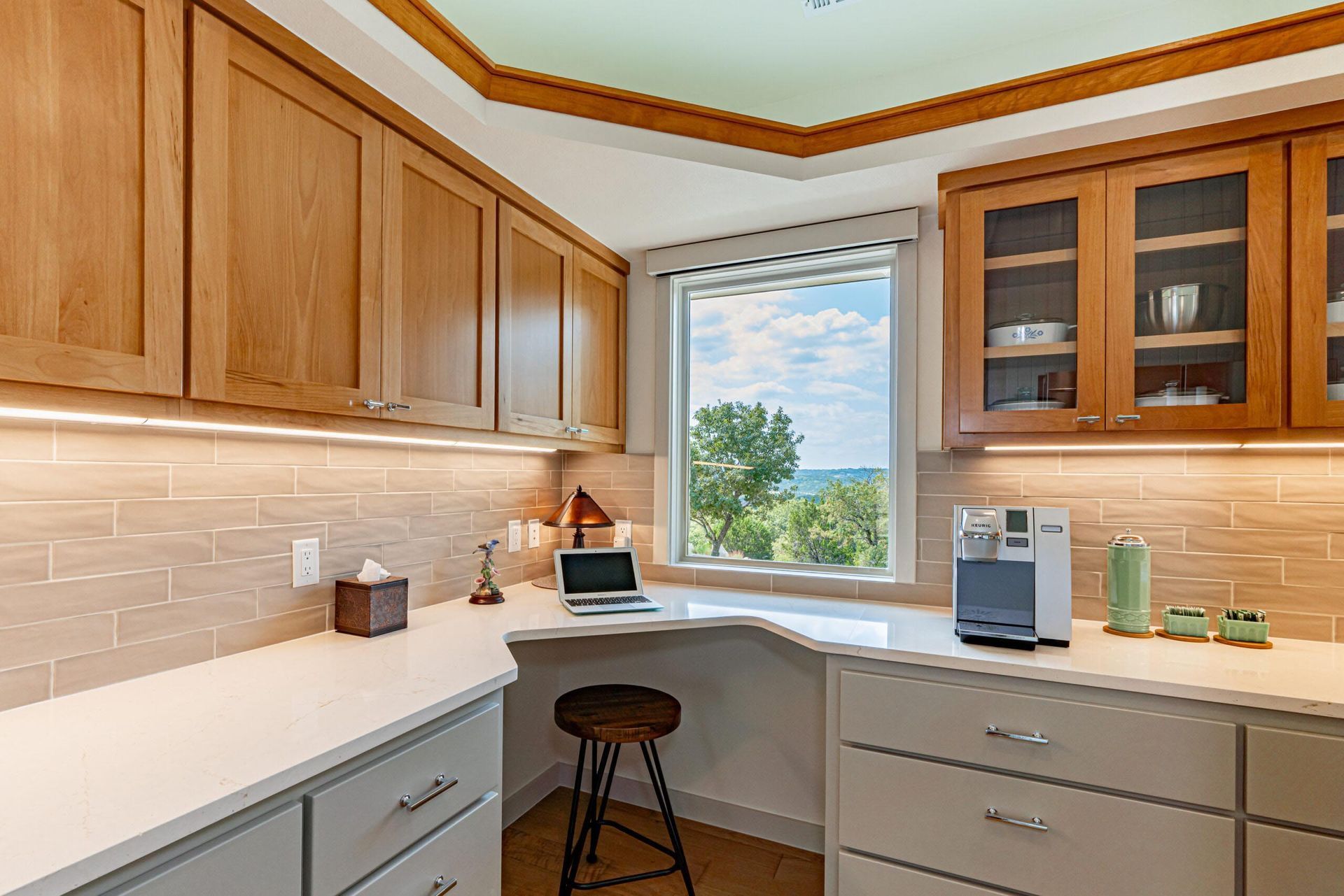 Home office nook with cabinets, desk, window with outdoor view, and a stool.